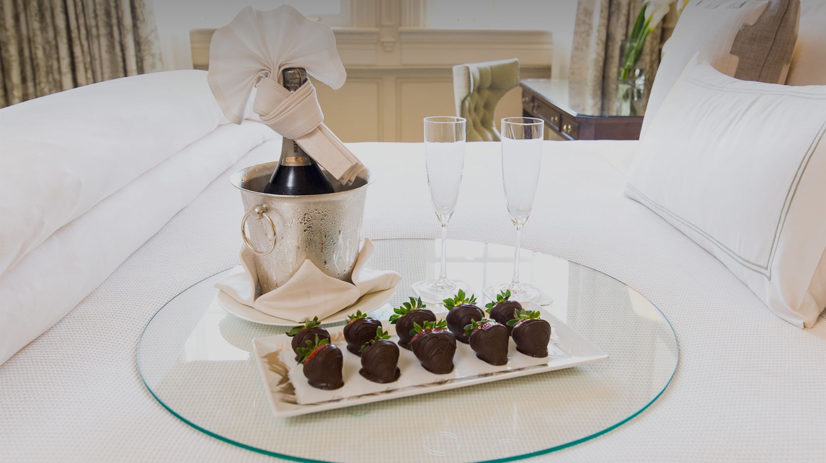 a tray of chocolate covered strawberries and champagne with two flutes sitting on a bed