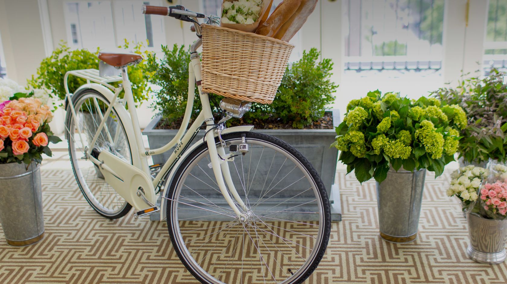 a bicycle with basket sitting in a room with vases of flowers